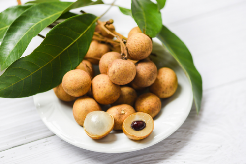 Displaying the tropical fruit longan on a plate behind some leaves.