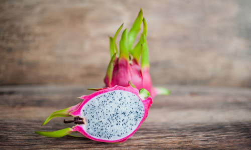 A whole dragon fruit and half a cut-up dragon fruit situated on a wooden table