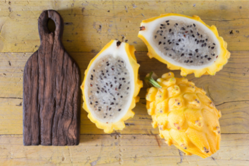 Sliced and whole yellow dragon fruit with a wooden cutting board, positioned on a wooden table.