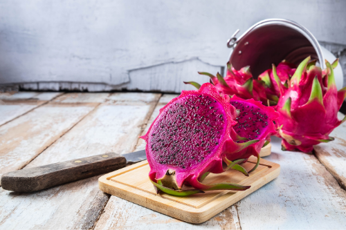 Sliced and whole purple dragon fruit on a wooden cutting board.