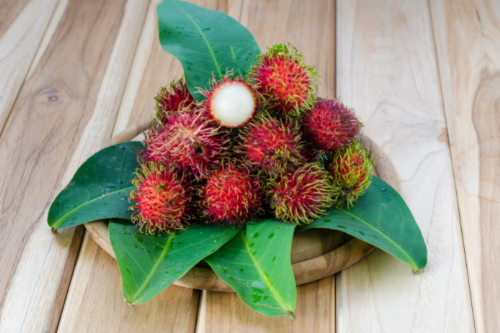 Rambutans laying on leaves, displaying on a wooden table