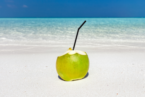 Green young coconut on a white beach, incredibly healthy drink