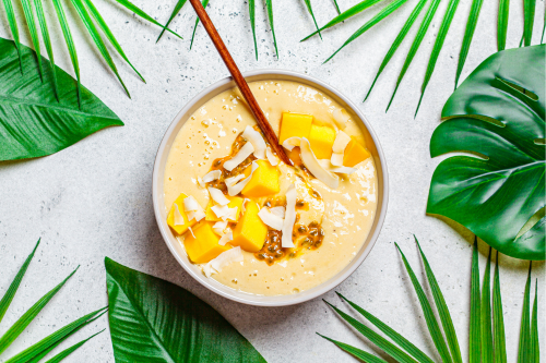 Tropical papaya smoothie bowl on a table with palm tree leaves around